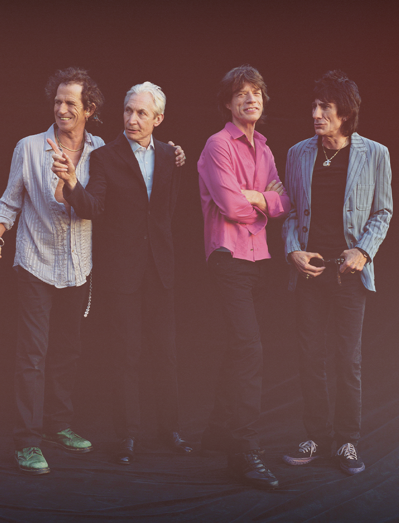 Four men (The Rolling Stones) standing together with a dark background