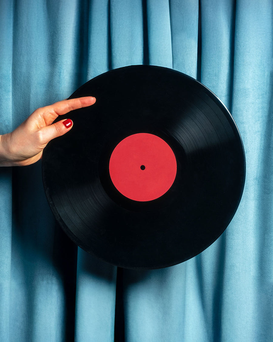 Vinyl record held by a hand with a cassette tape, against a blue curtain background, featuring the 'UMUSIC' logo.